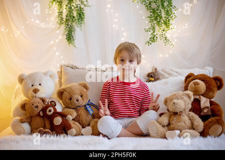 Süßer Vorschuljunge, der mit weißen und roten Armbändern spielt. Martenitsa, weiße und rote Garnstränge, bulgarische Folkloretradition, einladend für den Frühling Stockfoto