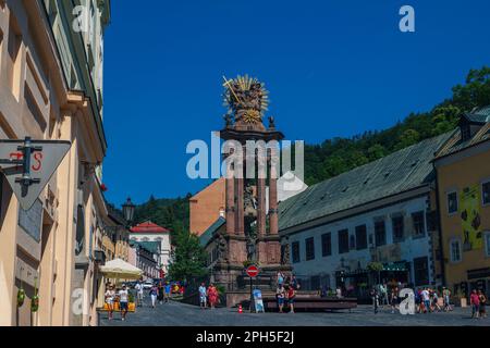 Banska Stiavnica, Slowakei - 14. August 2021: Blick auf die monumentale Pestsäule am Trinity Square über dem blauen Himmel, alte historische Architektur und Touristen Stockfoto