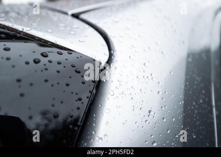Nahaufnahme, flacher Fokus von Süßwassertröpfchen auf der Metallic-Lackierung eines Hybrid-Stadtfahrzeugs. Zeigt einen Teil des schwarzen hinteren Dachspoilers. Stockfoto
