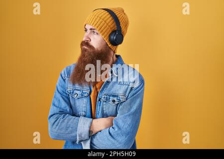 Weißer Mann mit langem Bart, der Musik mit Kopfhörern hört und zur Seite blickt, mit gestreuten Armen überzeugt und selbstbewusst Stockfoto