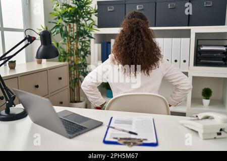 Junge hispanische Frau trägt Ärztin Uniform und Stethoskop rückwärts stehend Wegschauen mit Armen am Körper Stockfoto