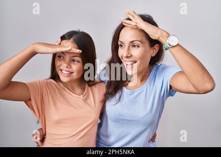 Junge Mutter und Tochter, die über weißem Hintergrund standen, waren sehr glücklich und lächelten weit weg mit Hand über Kopf. Suchbegriff. Stockfoto