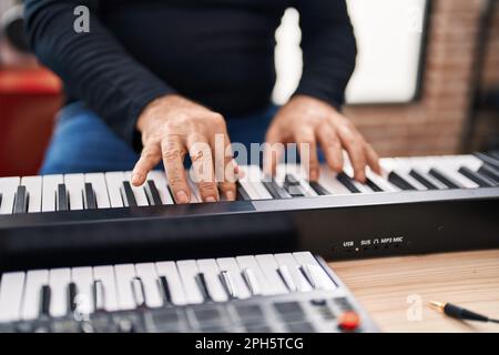 Ein grauhaariger Mann im mittleren Alter, der Klavier im Musikstudio spielt Stockfoto