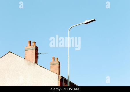 Straßenlaterne und zwei Schornsteintöpfe auf einem Terrassenhaus in einer typisch britischen Straße an einem sonnigen Morgen mit klarem blauen Himmel. Minimalistisch, abstrakt Stockfoto