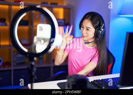 Junge chinesin nimmt Vlog-Tutorial mit Smartphone zu Hause auf, macht ein gutes Zeichen mit den Fingern, lächelnd freundlich Gesten ausgezeichnetes Symbol Stockfoto