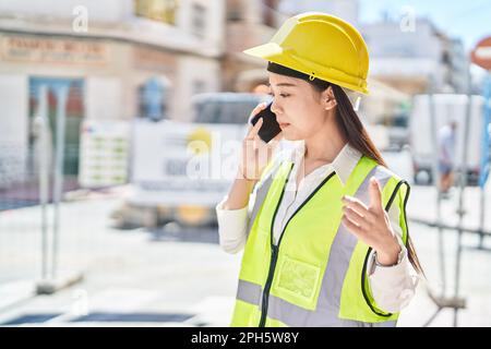 Junge chinesische Architektin, die auf der Straße mit einem Smartphone spricht Stockfoto