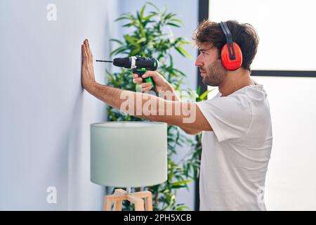 Junger Mann, der zu Hause eine Wand bohrt Stockfoto
