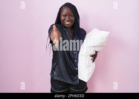 Junge afrikanische Frau mit Pijama-Kissen, die freundlich lächelt und als Begrüßung und Begrüßung einen Händedruck anbietet. Erfolgreiches Geschäft. Stockfoto