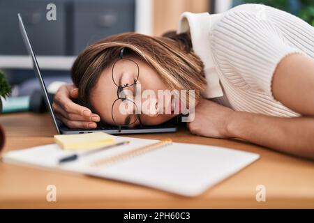 Junge, wunderschöne hispanische Frau, Geschäftsfrau, die im Büro mit dem Kopf auf dem Laptop schläft Stockfoto