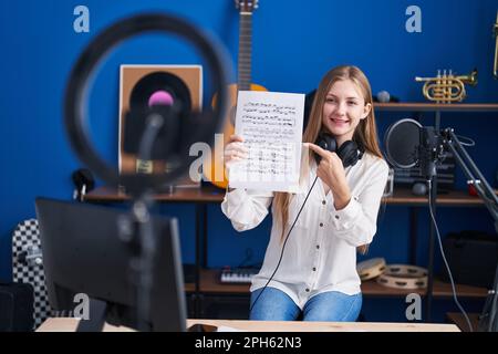 Junge weiße Frau, die Online-Musik-Tutorial macht und ein Lächeln zeigt, die glücklich mit der Hand und dem Finger zeigt Stockfoto