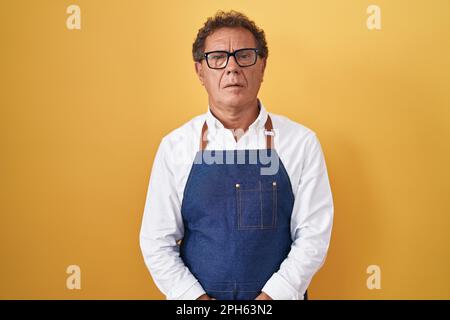hispanischer Mann im mittleren Alter mit professioneller Kochschürze, entspannt mit ernstem Gesichtsausdruck. Einfaches und natürliches Betrachten in die Kamera. Stockfoto
