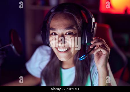 Junge schöne hispanische Frau streamer lächelnd selbstbewusst auf dem Tisch im Spielzimmer sitzen Stockfoto