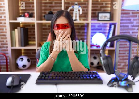 Eine chinesin mittleren Alters, die eine Virtual-Reality-Brille trägt, die den Mund mit Händen verdeckt. Geheimes Konzept. Stockfoto