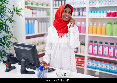 Eine junge, schöne Apothekerin, die telefoniert, indem sie einen Computer in der Apotheke benutzt Stockfoto