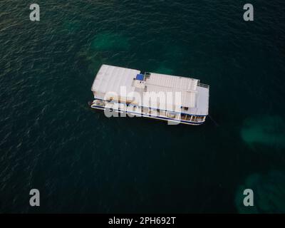 Blick von oben. Vergnügungsboot auf dem Meer. Auf dem smaragdgrünen Wasser ein weißes Boot. Spaziergänge auf dem Meer, Erholung, Reisen, Tourismus. Stockfoto