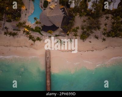 Luftaufnahme. Holzpier, Strand, Meer. Am Sandstrand gibt es Strohschirme, tropische Pflanzen, Palmen. Resort. In der Entfernung sehen Sie t Stockfoto