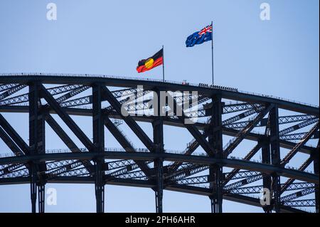 Vor einem blauen Himmel fliegt die Flagge der Aborigines neben der australischen Flagge auf der Sydney Harbour Bridge, New South Wales, Australien. Stockfoto