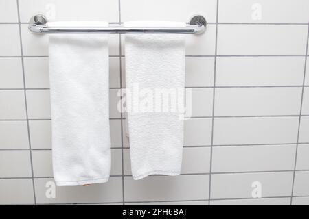 Beheizter Handtuchhalter an der Badezimmerwand. Weiße Handtücher trocknen auf einem beheizten Handtuchhalter Stockfoto