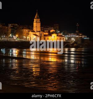 Alte Steinkirche am Meer bei Nacht mit Reflexionen im Wasser, Gijon, Asturien. Stockfoto