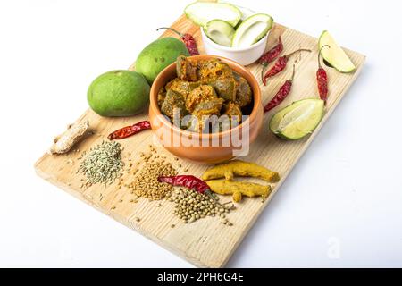 Indische Mangogurke mit grünen Mangoscheiben und Gewürzen mit brauner Schüssel auf Holzbrett Stockfoto