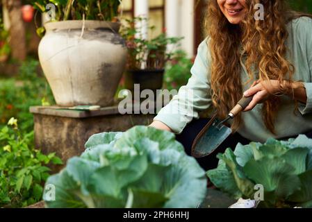 Junge Gärtnerin mit Gärtnerkelle im Strohhut, die sich um grüne Topfpflanzen kümmert – Nahaufnahme. Junge weiße Frau lächelt im Garten Stockfoto