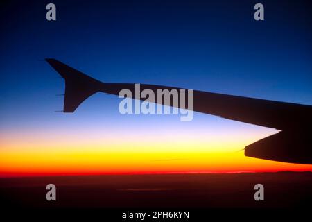 Silhouette eines Flugzeugflügels während des Fluges über Zentralfrankreich bei Sonnenuntergang im Winter. Stockfoto