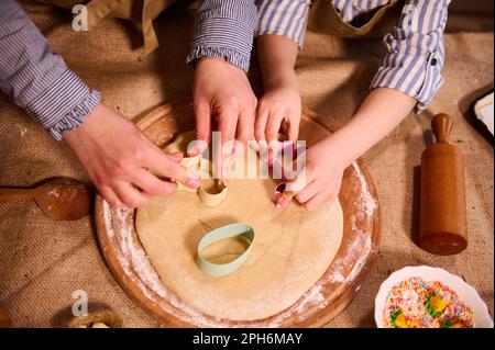 Die Hände von mutter und Kind legen die Keksschneider auf den Teig und bereiten hausgemachtes Lebkuchen für die Osterferien zu Stockfoto