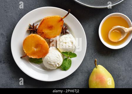 Pochierte Birnen mit Eiscreme auf dem Teller auf dunklem Steinhintergrund. Draufsicht, flach liegend Stockfoto