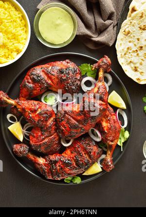 Tandoori-Hühnchen im indischen Stil auf dem Teller mit dunklem Steinhintergrund. Hähnchenschenkel mariniert in Joghurt und Gewürzen. Draufsicht, flach liegend Stockfoto