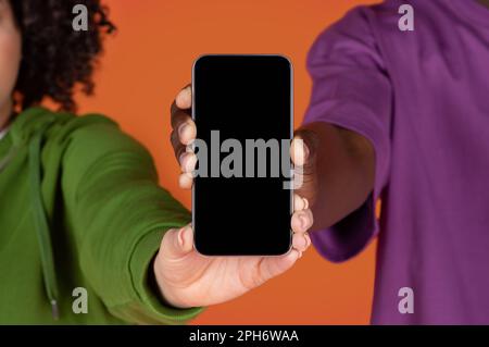 Nicht erkennbares, multirassisches Paar, das ein Telefon mit leerem Bildschirm hält Stockfoto