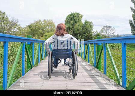 Rückansicht einer unbekannten Frau, die im Rollstuhl im Freien spaziert. Stockfoto