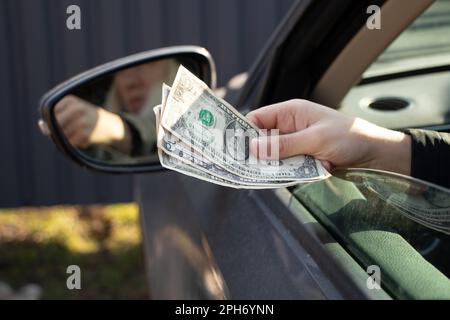 Die Hand einer Frau zieht eine Dellara aus einem Autofenster, Korruption und Bestechung auf der Straße Stockfoto
