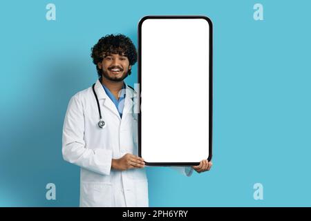 Positiver indischer Familienarzt, der ein riesiges Smartphone in der Hand hat Stockfoto