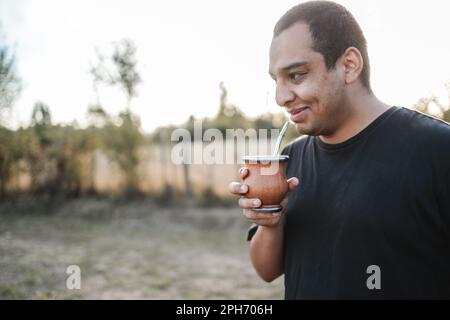 Lächelnder junger latino, der bei Sonnenuntergang Yerba-Mate trinkt. Speicherplatz kopieren Stockfoto