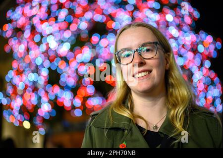 Die Bokeh-Schönheit unscharfer Weihnachtslichter schafft den perfekten Hintergrund für dieses Porträt einer glücklichen und eleganten Frau, die das Festival genießt Stockfoto