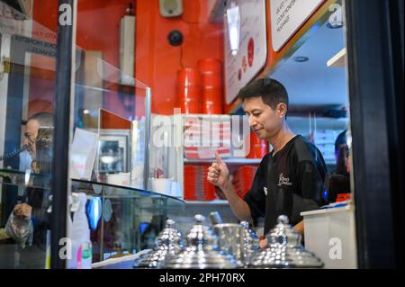 LONDON - 12. November 2022: Werfen Sie einen Blick hinter die Kulissen eines Keksladens und sehen Sie einen Mann bei der Arbeit durch das Schaufenster, der Delikatessen zubereitet Stockfoto