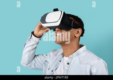 Der fröhliche Millennials-Schwarze in lässiger und VR-Brille schaut auf leeren Raum und liebt Online-Spiele Stockfoto