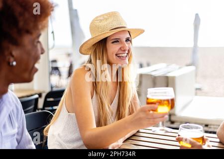 Fröhliche junge Millennial-Freunde jubeln mit kaltem Bier auf der Terrasse der Strandbar. Stockfoto