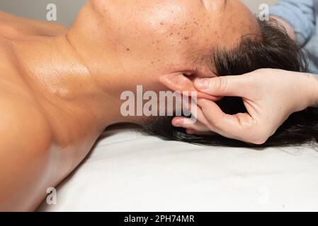 Massagetherapeut starke Hände und Daumen halten die Ohren des Patienten für sofortige Schmerzlinderung an. Stockfoto