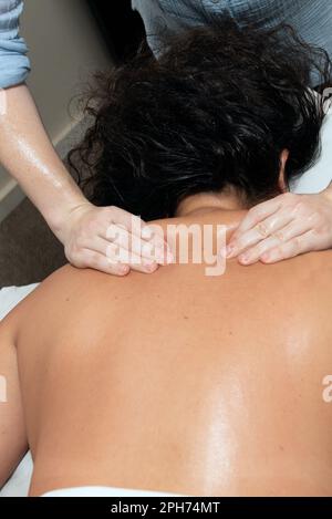 Masseur starke Hände und Daumen graben sich tief in die oberen Rückenmuskeln, um Schmerzen sofort zu lindern. Stockfoto