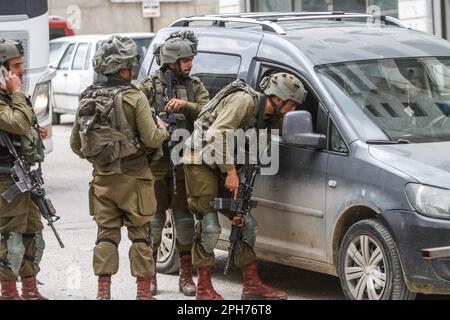 Nablus, Palästina. 26. März 2023. Israelische Soldaten durchsuchen palästinensische Autos nach einem Schussanschlag auf zwei israelische Soldaten in der Stadt Hawara südlich von Nablus im besetzten Westjordanland. Unruhen zwischen Palästinensern, jüdischen Siedlern und israelischen Soldaten in der Stadt Hawara, nachdem die Siedler ein hartes Vorgehen gegen Palästinenser forderten, nachdem ein Palästinenser das Feuer auf einen Militärposten eröffnete und zwei israelische Soldaten verletzte. Das ist der dritte Schussanschlag in der Stadt diesen Monat. Kredit: SOPA Images Limited/Alamy Live News Stockfoto