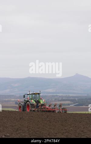 Ein grüner Fendt-Traktor mit einem wendbaren Pflug, der auf einem Pflügen in Aberdeenshire an einem Kverneland-Doppelpacker mit Bennachie in der Ferne folgt Stockfoto