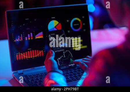 Nahaufnahme einer modernen Frau mit Laptop und Smartphone, die in einem modernen Büro eine Börsenanalyse und einen wirtschaftlichen Finanzbericht prüft. Stockfoto