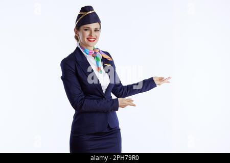 Fröhliche, stilvolle Flugbegleiterin vor weißem Hintergrund in Uniform einladend. Stockfoto