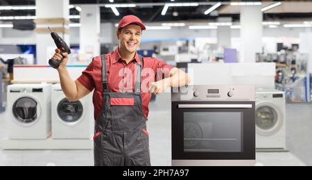 Ein Techniker mit einer Elektrobohrmaschine steht neben einem Ofen in einer Haushaltswerkstatt Stockfoto