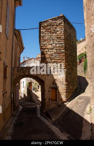 Eine schmale Gasse führt durch eines der verbleibenden Tore der mittelalterlichen Stadtmauer des alten Dorfes Roquebrun in Südfrankreich Stockfoto