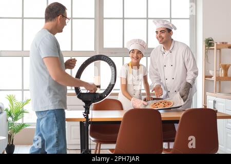 Glücklicher kleiner Junge mit seinem Vater und Großvater, der Kochvideo in der Küche aufnimmt Stockfoto