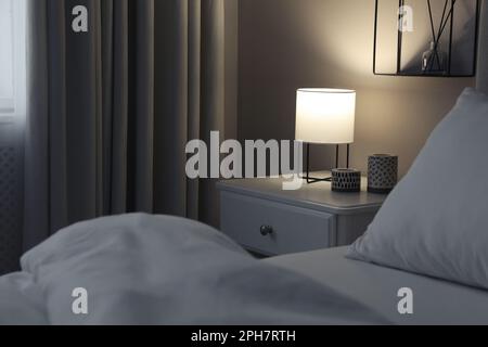 Stilvolle Lampe und Kerzen auf weißem Nachttisch im Schlafzimmer Stockfoto