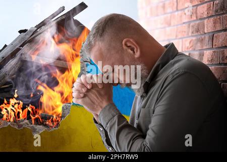 Ein verärgerter Seniorenmann nahe der Wand eines zerstörten Gebäudes, in Farbe der Nationalflagge auf Feuer gemalt. Beenden Sie den Krieg in der Ukraine Stockfoto