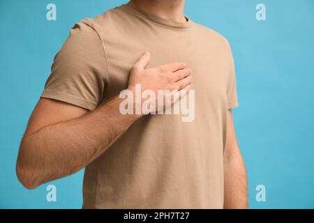 Ein Mann, der die Hand nahe der Brust hält, auf türkisfarbenem Hintergrund, Nahaufnahme Stockfoto